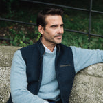 Man wearing a Darzi Midnight Blue merino wool waistcoat sitting on a stone wall with a blurred background