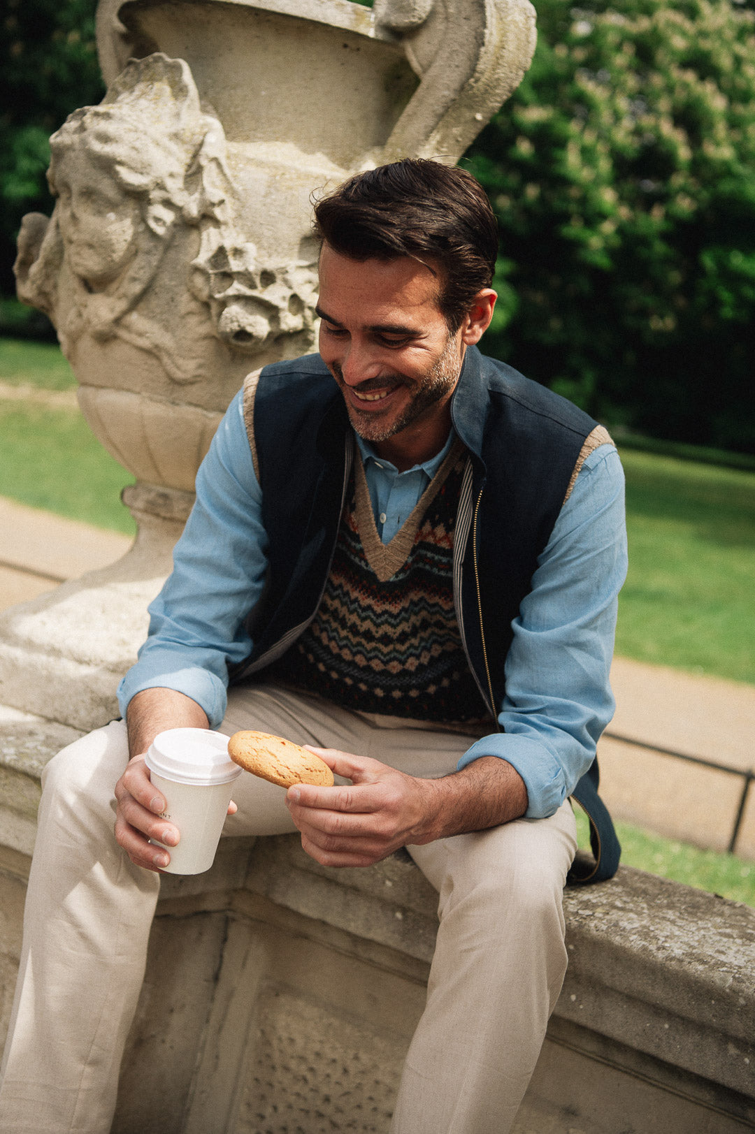 Man sitting outdoors drinking from a cup of coffee wearing a Darzi navy linen Hillgate gilet