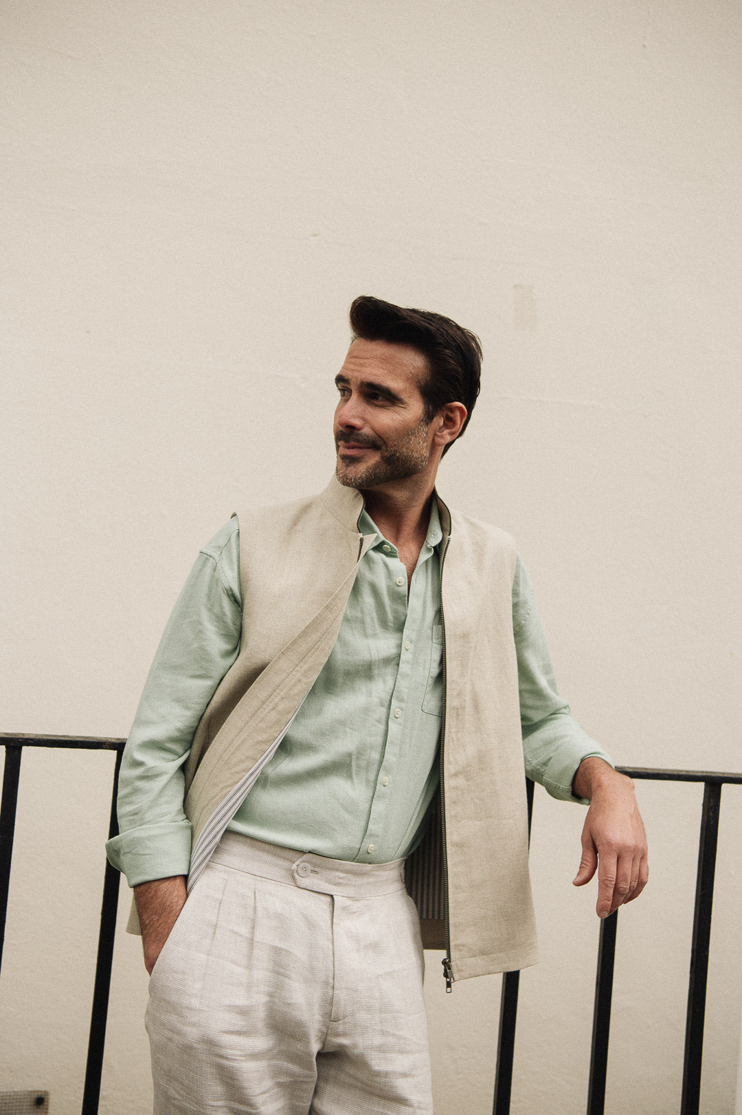 Man wearing a light green shirt and beige linen vest against a plain background