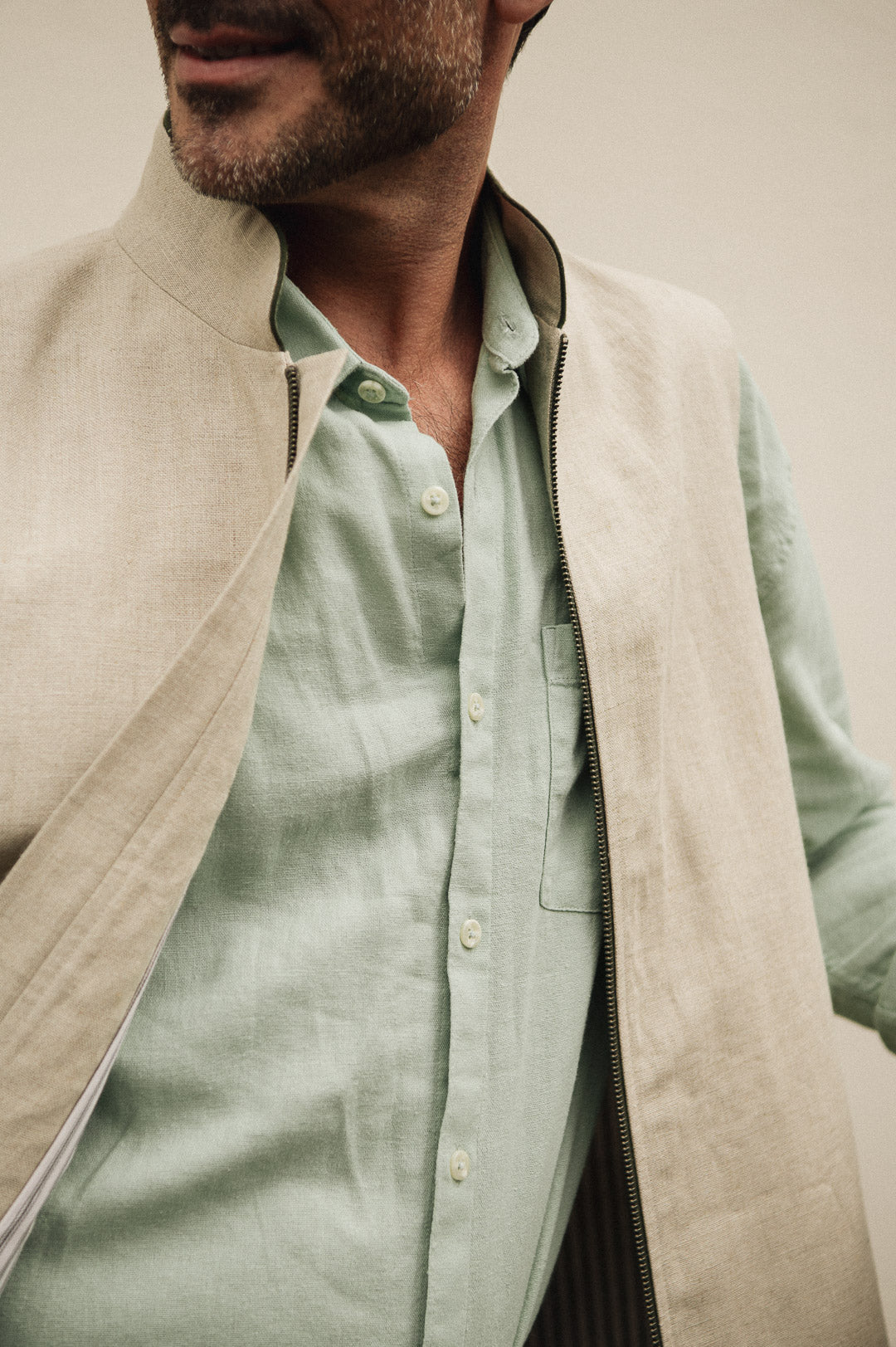 Man wearing a light green shirt and beige vest against a neutral background