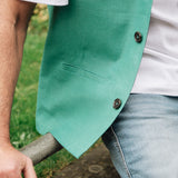 Person wearing a Darzi green linen waistcoat over a white shirt with a blurred natural background