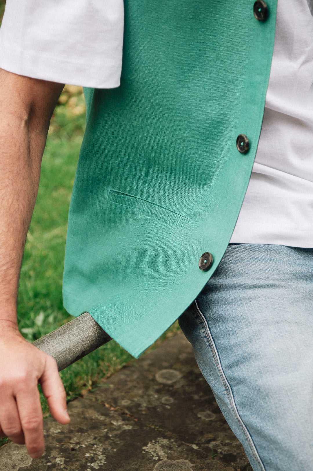 Person wearing a Darzi green linen waistcoat over a white shirt with a blurred natural background