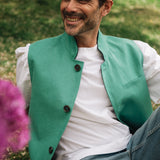 Man wearing a green Darzi linen vest over a white shirt, sitting outdoors with grass and flowers in the background.