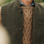 Man wearing a brown cable knit sweater under a dark green Darzi wool Helmsley waistcoat