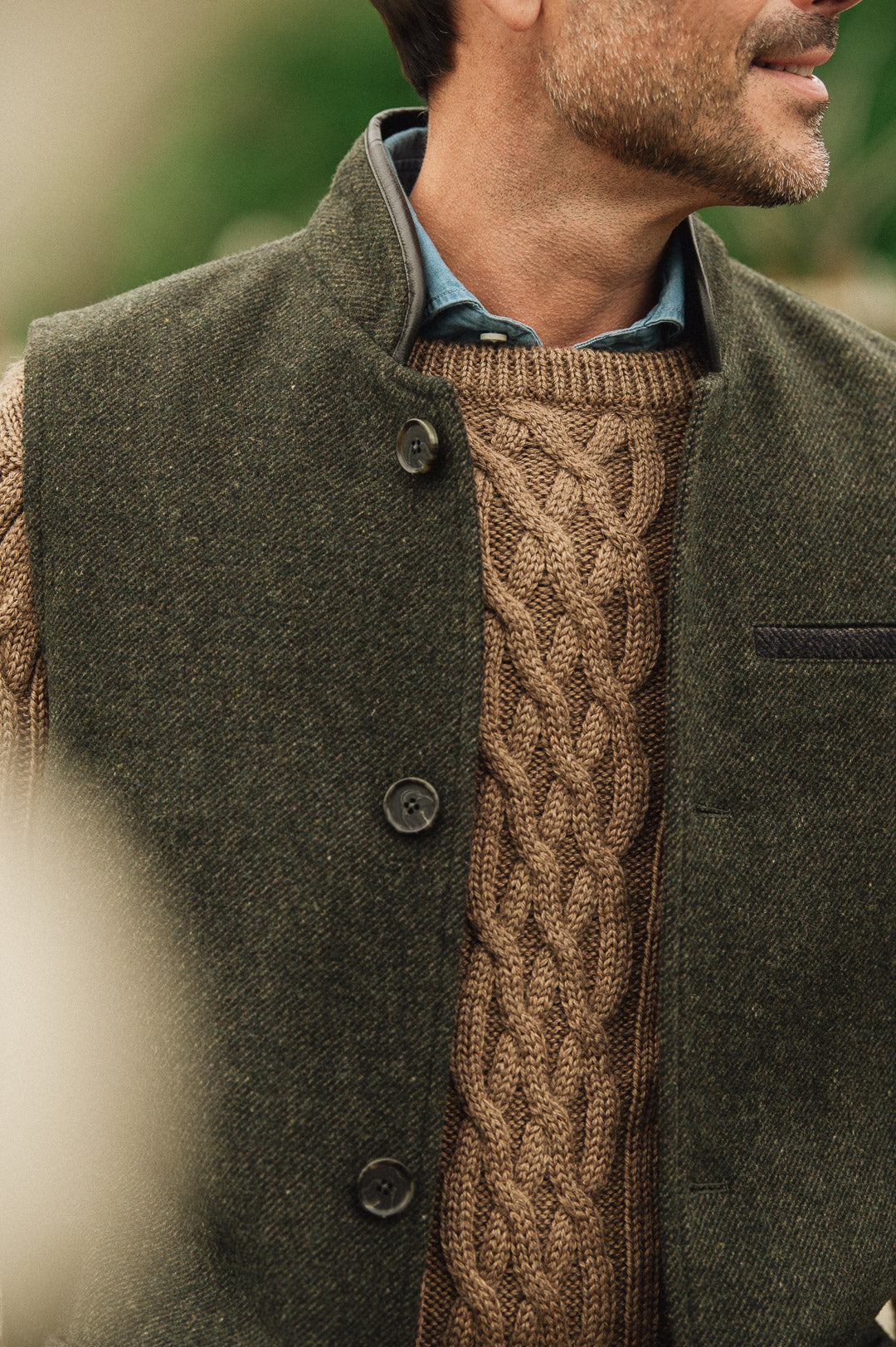 Man wearing a brown cable knit sweater under a dark green Darzi wool Helmsley waistcoat