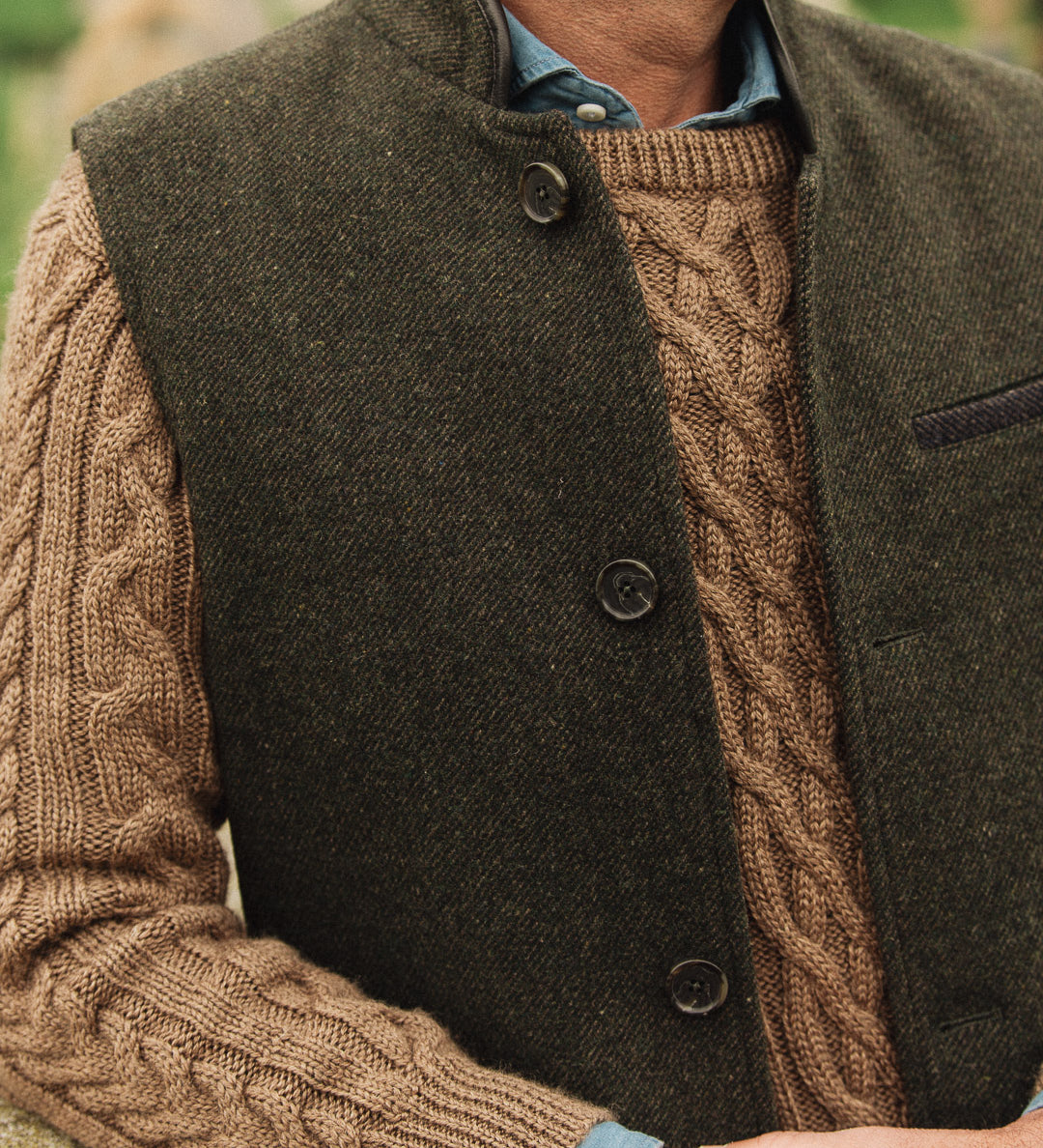 Man wearing a brown cable knit sweater under a dark green Darzi wool Helmsley waistcoat