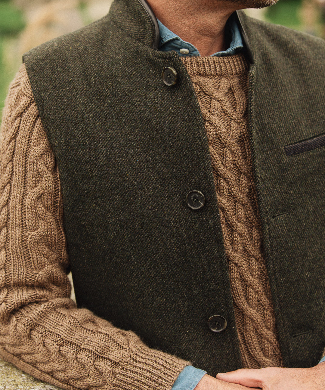 Man wearing a brown cable knit sweater under a dark green Darzi wool Helmsley waistcoat