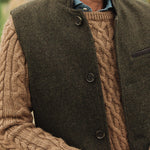 Man wearing a brown cable knit sweater under a dark green Darzi wool Helmsley waistcoat
