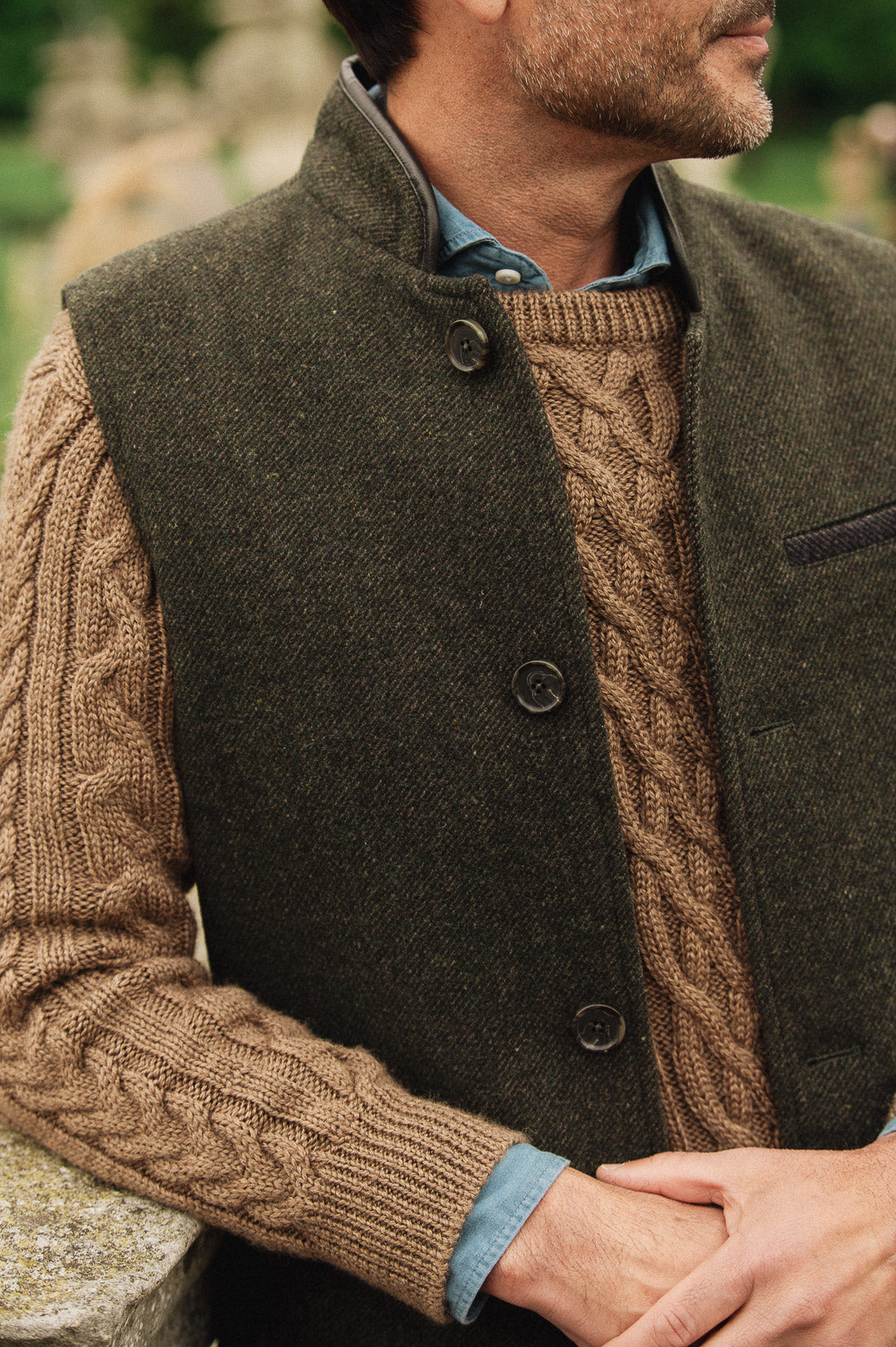 Man wearing a brown cable knit sweater under a dark green Darzi wool Helmsley waistcoat