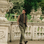 Man walking in a garden wearing a Darzi Helmsley wool waistcoat surrounded by Italianate  sculptures and greenery