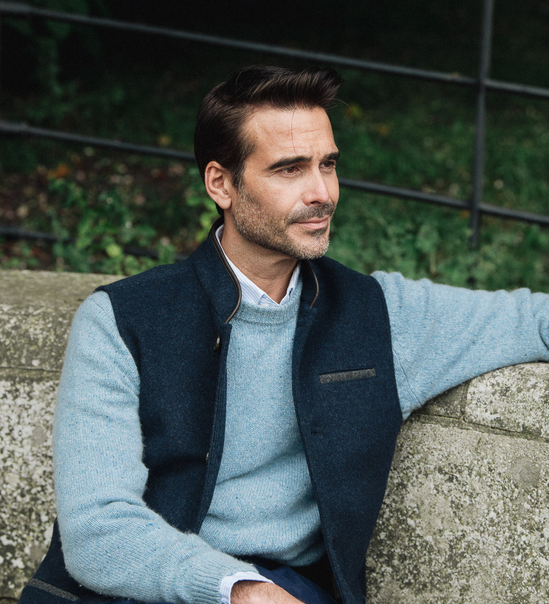 Man wearing a Darzi Midnight Blue merino wool waistcoat sitting on a stone wall with a blurred background