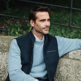 Man wearing a Darzi Midnight Blue merino wool waistcoat sitting on a stone wall with a blurred background