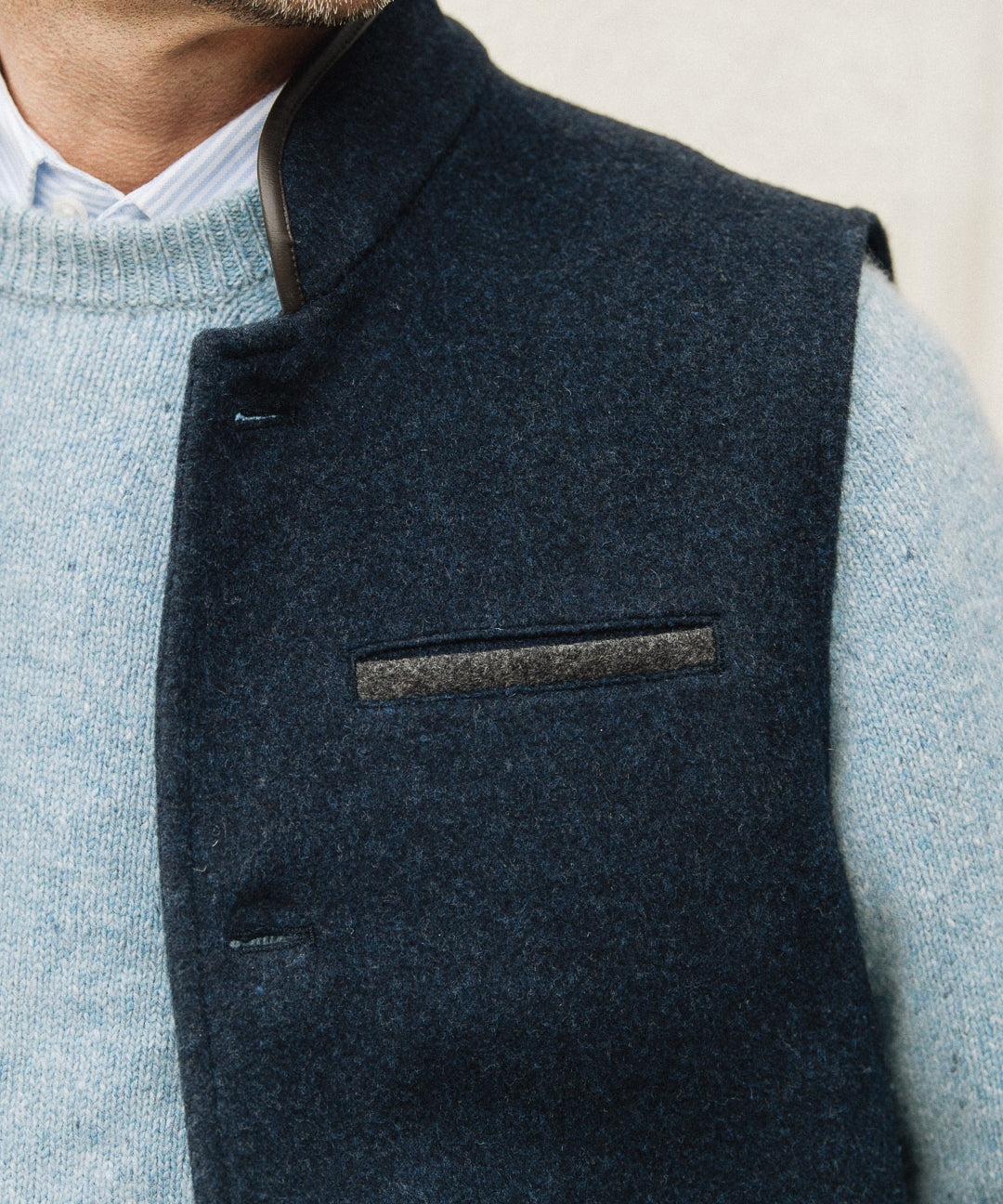 Man wearing a Darzi Midnight Blue merino wool waistcoat over light blue sweater against a neutral background