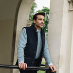 Man standing outdoors near a stone archway wearing a blue sweater and Darzi midnight blue merino vest