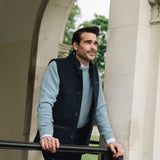 Man standing outdoors near a stone archway wearing a blue sweater and Darzi midnight blue merino vest