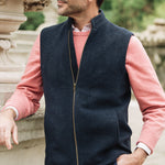 Man wearing a navy Darzi merino wool gilet over a pink sweater with a blurred natural background