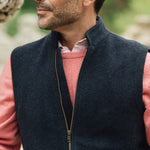 Man wearing a navy Darzi merino wool gilet over a pink sweater with a blurred natural background