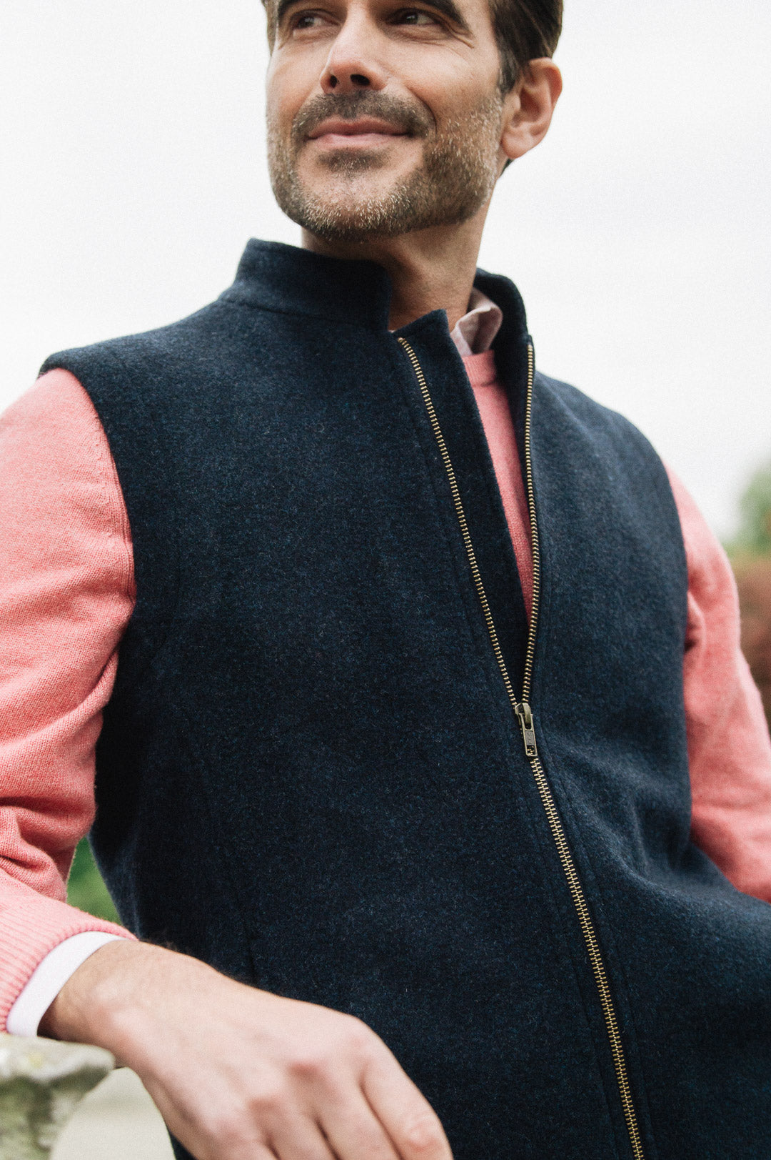 Man wearing a Darzi Hillgate heavyweight midnight blue merino wool gilet over a pink sweater