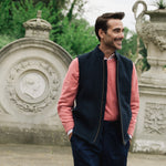 Man wearing a Darzi Hillgate heavyweight midnight blue merino wool gilet over a pink sweater in an Italian style garden setting