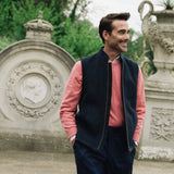 Man wearing a Darzi Hillgate heavyweight midnight blue merino wool gilet over a pink sweater in an Italian style garden setting