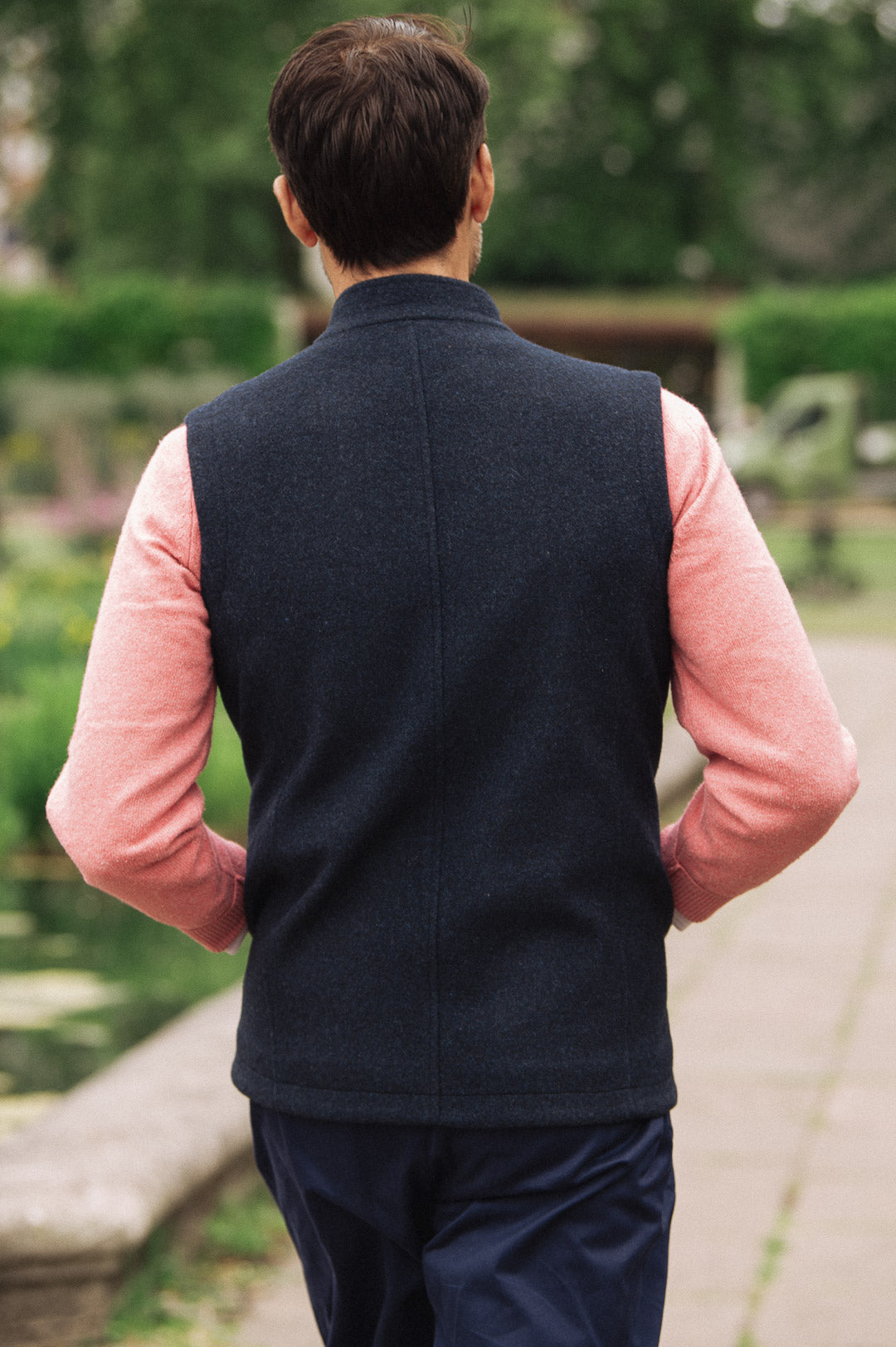 Man wearing a Darzi Hillgate heavyweight midnight blue merino wool gilet over a pink sweater - shown from behind