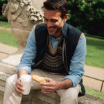 Man sitting outdoors drinking from a cup of coffee wearing a Darzi navy linen Hillgate gilet