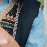 Person wearing a blue shirt, a Darzi navy linen Hillgate vest and patterned sweater with a blurred background