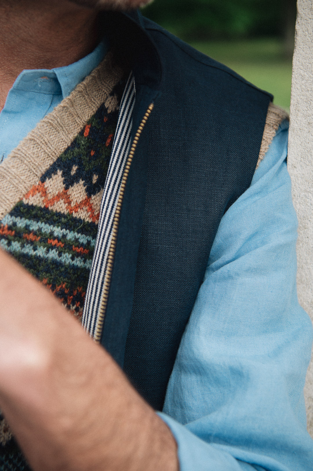Person wearing a blue shirt, a Darzi navy linen Hillgate vest and patterned sweater with a blurred background