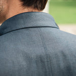 Back view of a person wearing a navy Darzi Hillgate linen vest with a blurred green outdoor background