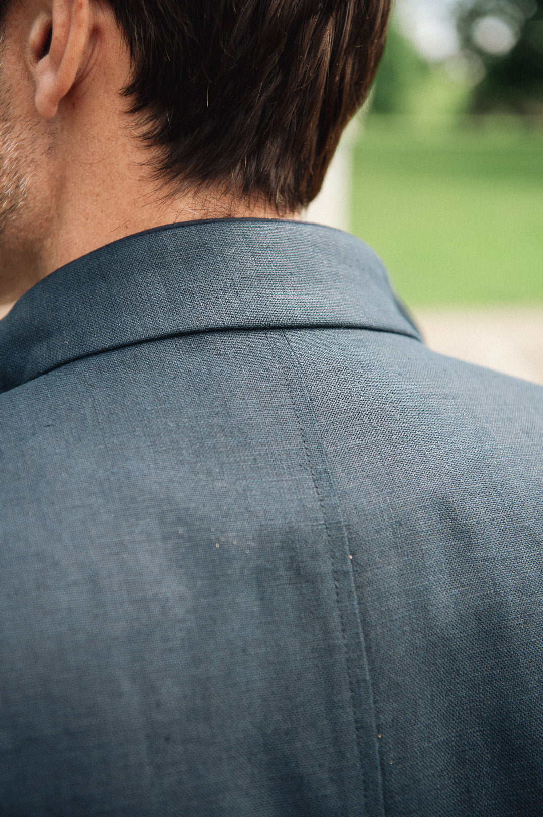 Back view of a person wearing a navy Darzi Hillgate linen vest with a blurred green outdoor background