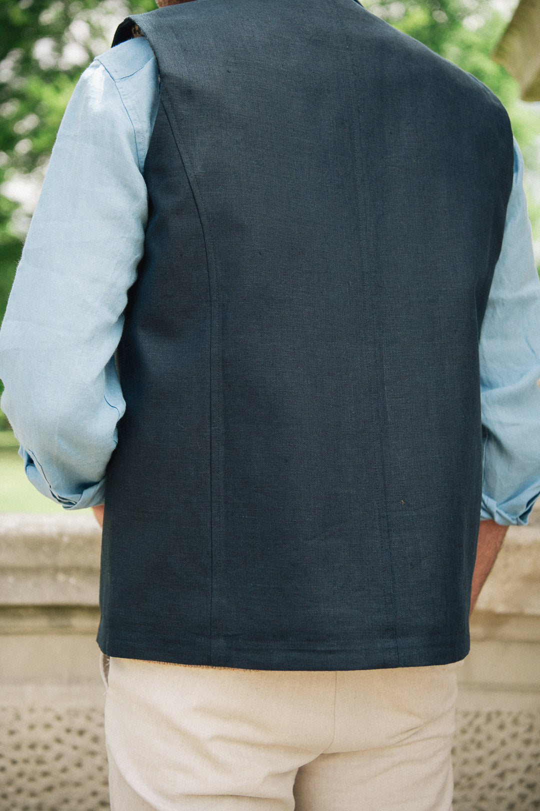 Person wearing a Darzi navy linen Hillgate gilet over a light blue shirt with beige pants, standing outdoors.