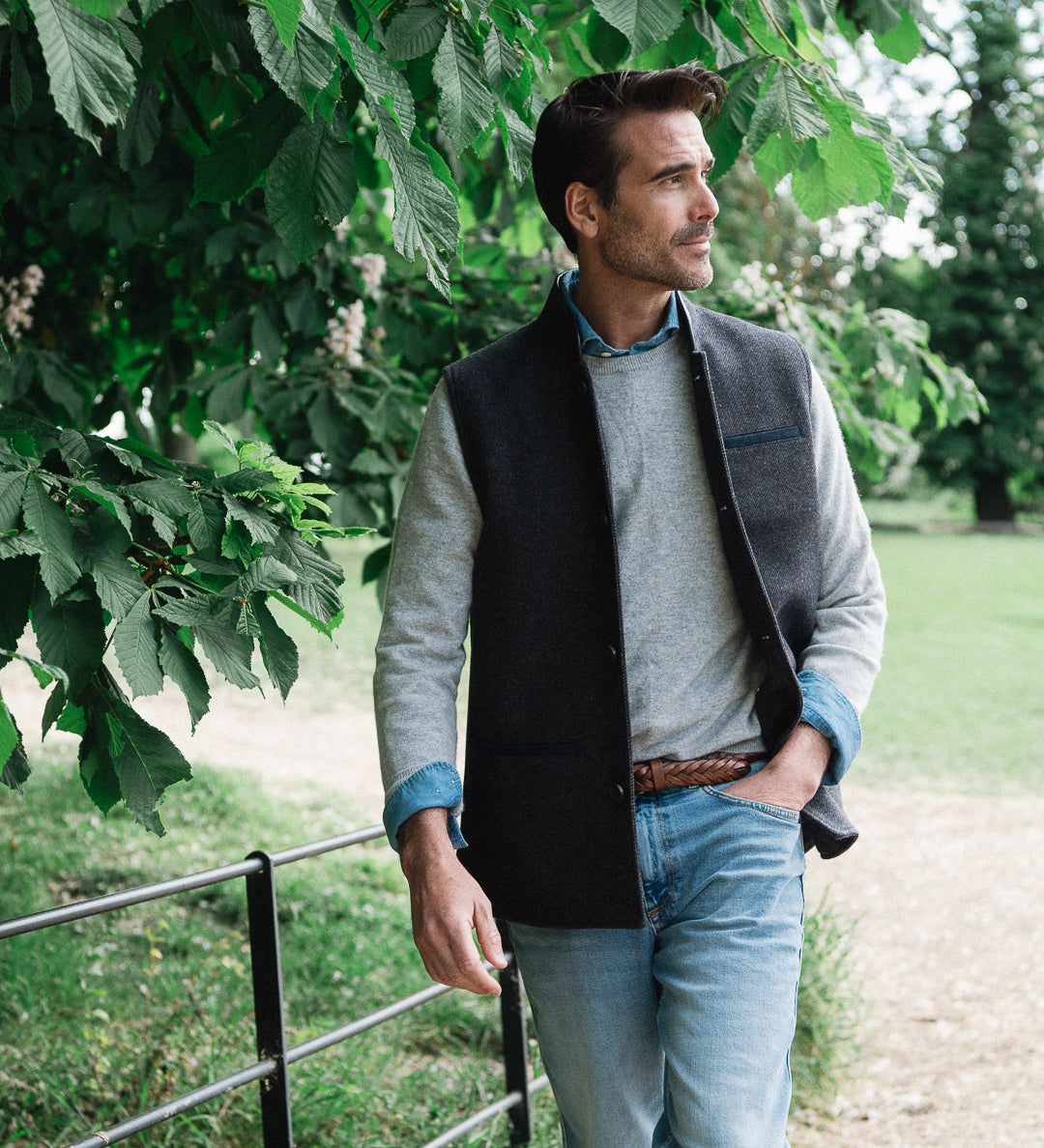 Man standing outdoors under a tree wearing a Darzi wool waistcoat, the Helmsley in Blue Brown Twill
