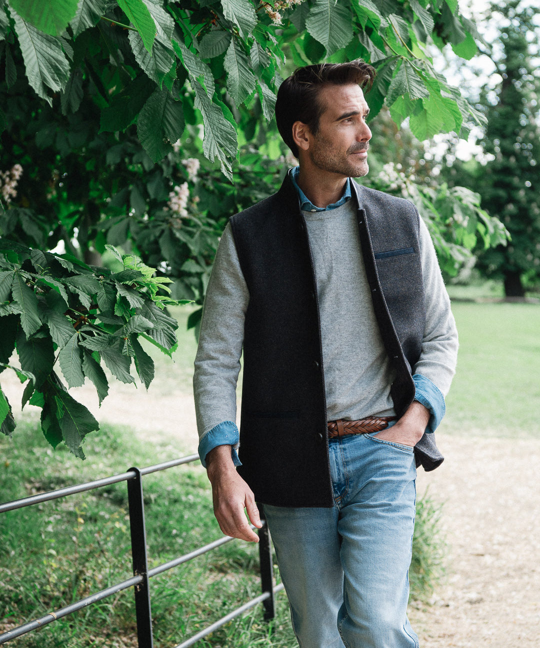 Man standing outdoors under a tree wearing a Darzi wool waistcoat, the Helmsley in Blue Brown Twill