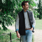Man standing outdoors under a tree wearing a Darzi wool waistcoat, the Helmsley in Blue Brown Twill