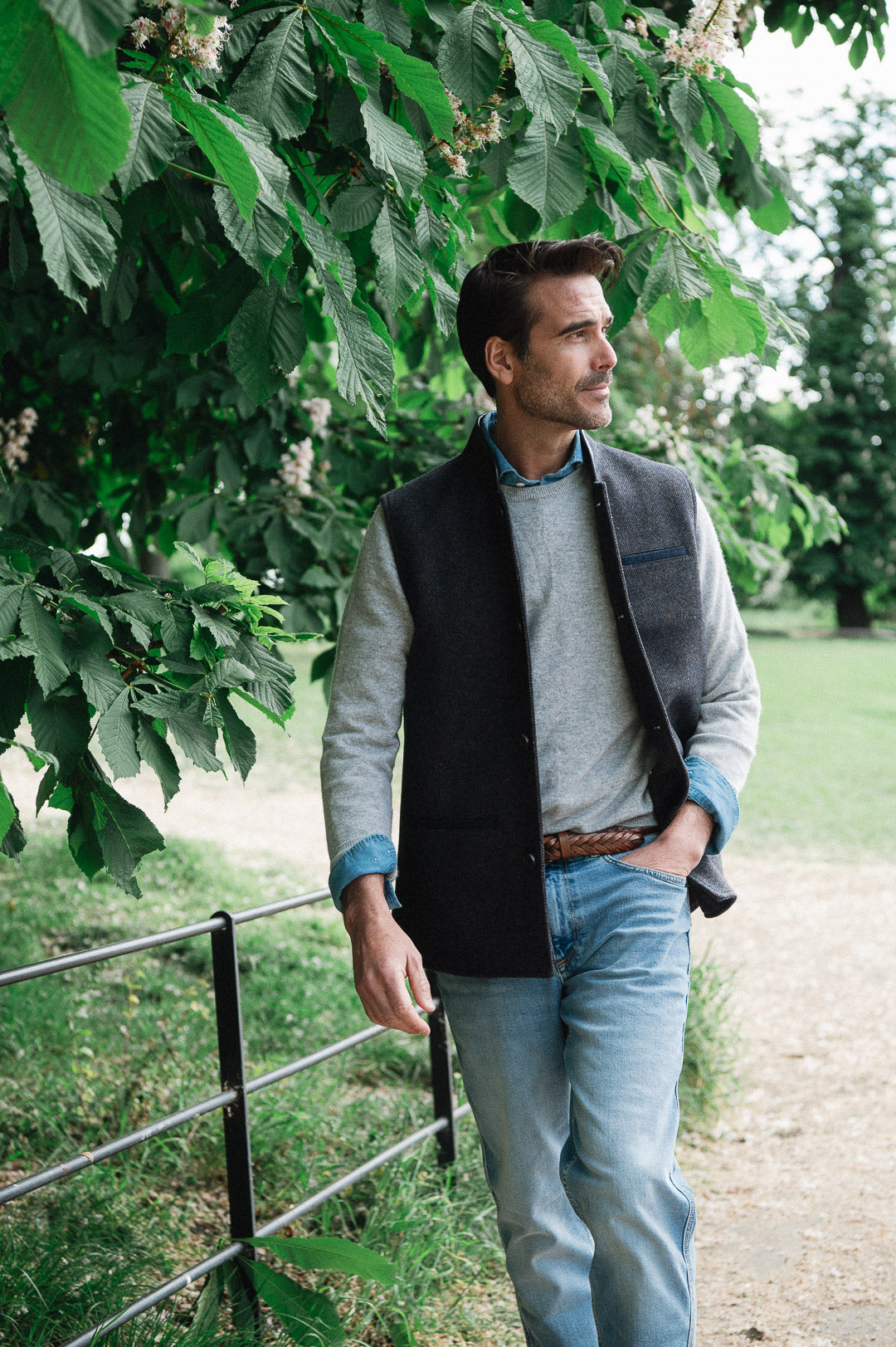 Man standing outdoors under a tree wearing a Darzi wool waistcoat, the Helmsley in Blue Brown Twill