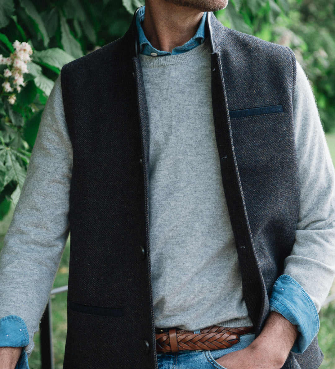 Man standing outdoors wearing a Darzi Helmsley wool waistcoat in Blue Brown Twill over a grey sweater, with jeans