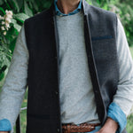Man standing outdoors wearing a Darzi Helmsley wool waistcoat in Blue Brown Twill over a grey sweater, with jeans