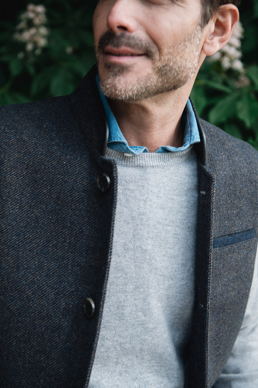 Man standing outdoors wearing a Darzi Helmsley wool waistcoat in Blue Brown Twill over a grey sweater