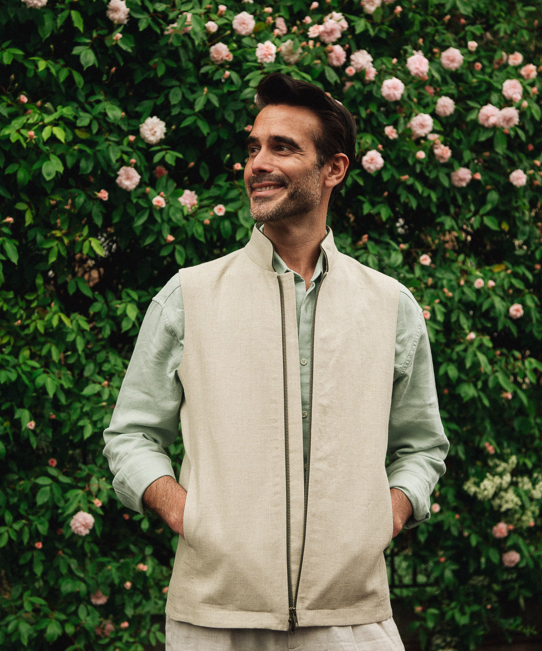 Man wearing a Darzi limestone linen Hillgate gilet standing in front of a rose bush