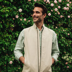 Man wearing a Darzi limestone linen Hillgate gilet standing in front of a rose bush