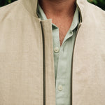 Close-up of a man wearing a Darzi limestone linen Hillgate gilet over a light green shirt with a blurred green background