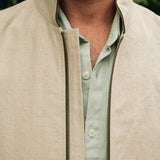 Close-up of a man wearing a Darzi limestone linen Hillgate gilet over a light green shirt with a blurred green background