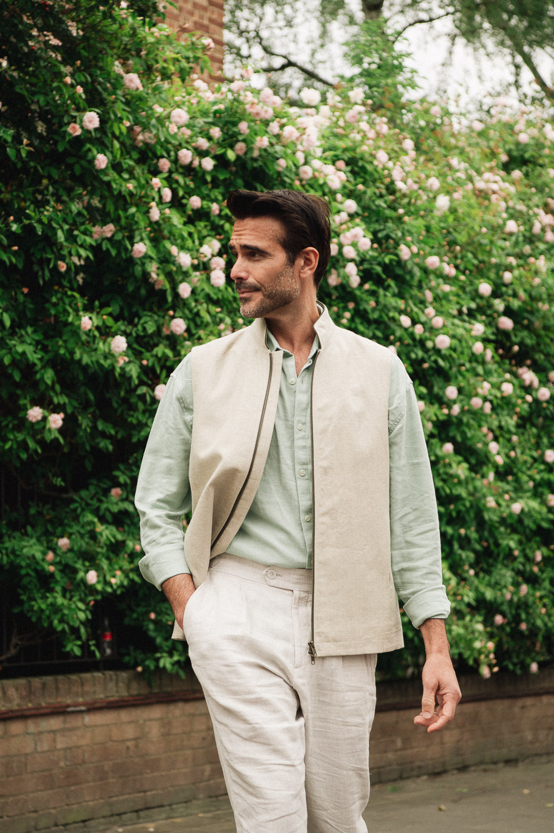 Man in light-colored linen gilet in front of rose bush