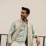 Man wearing a light green shirt and beige linen vest against a plain background