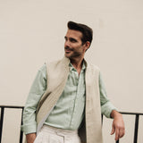 Man wearing a light green shirt and beige linen vest against a plain background