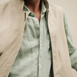 Man wearing a light green shirt and beige vest against a neutral background