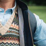 Person wearing a patterned jumper over a light blue shirt, under a Darzi navy linen Hillgate gilet with a blurred green background