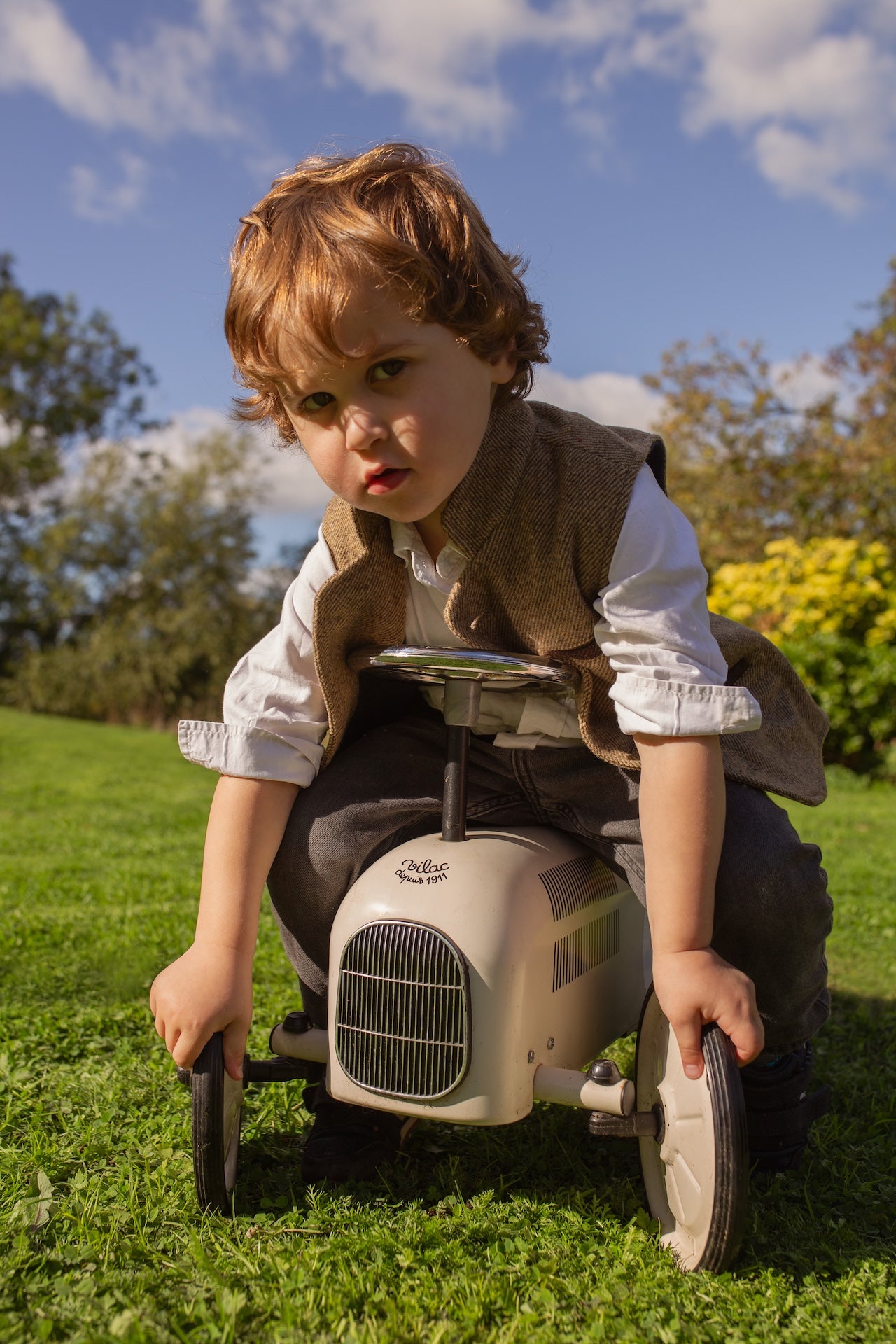 Little boy sitting on toy car wearing a Little Darzi Camel Brown wool waistcoat