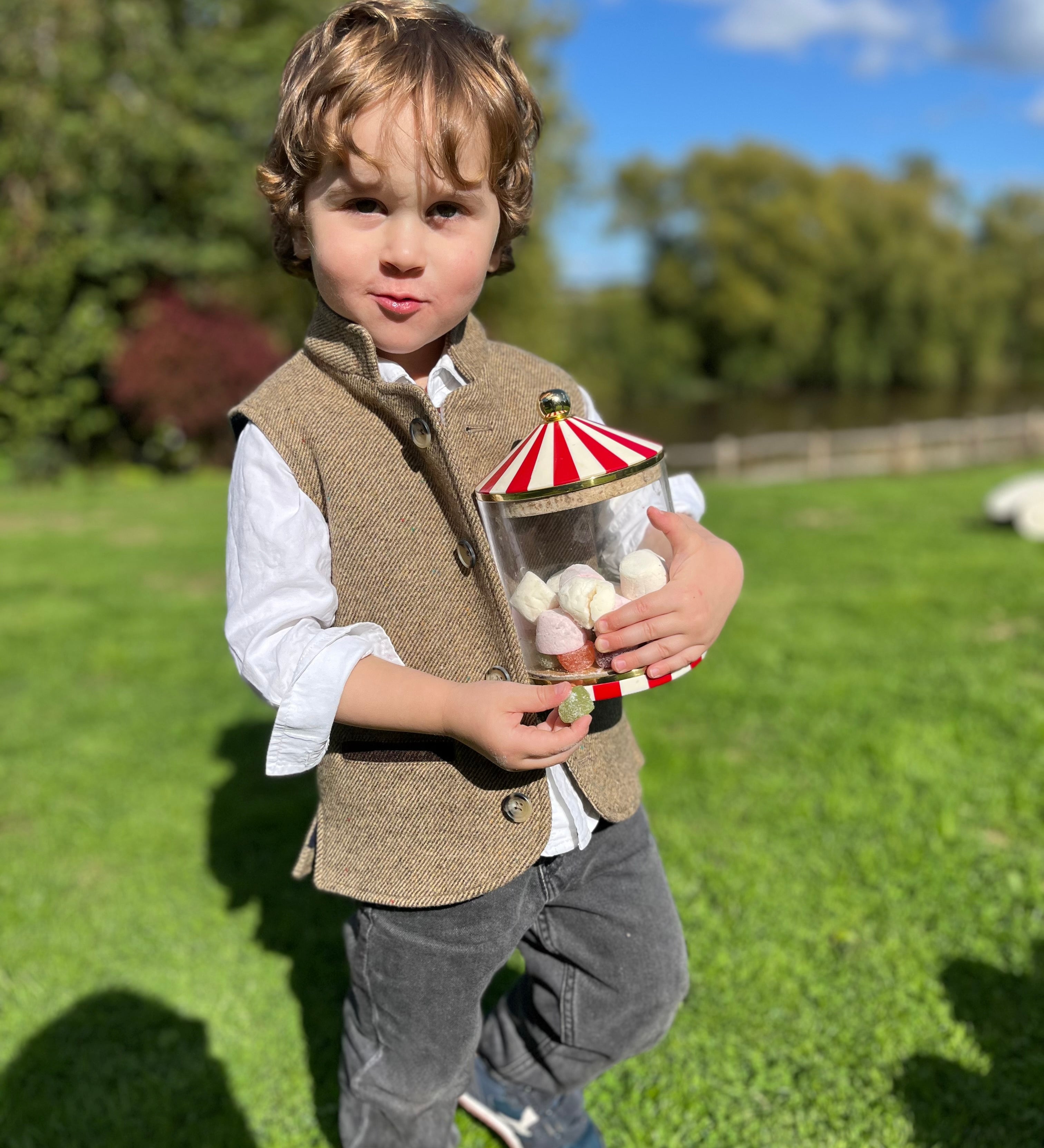 Boy wearing Little Darzi gilet in Camel Brown holding candy jar