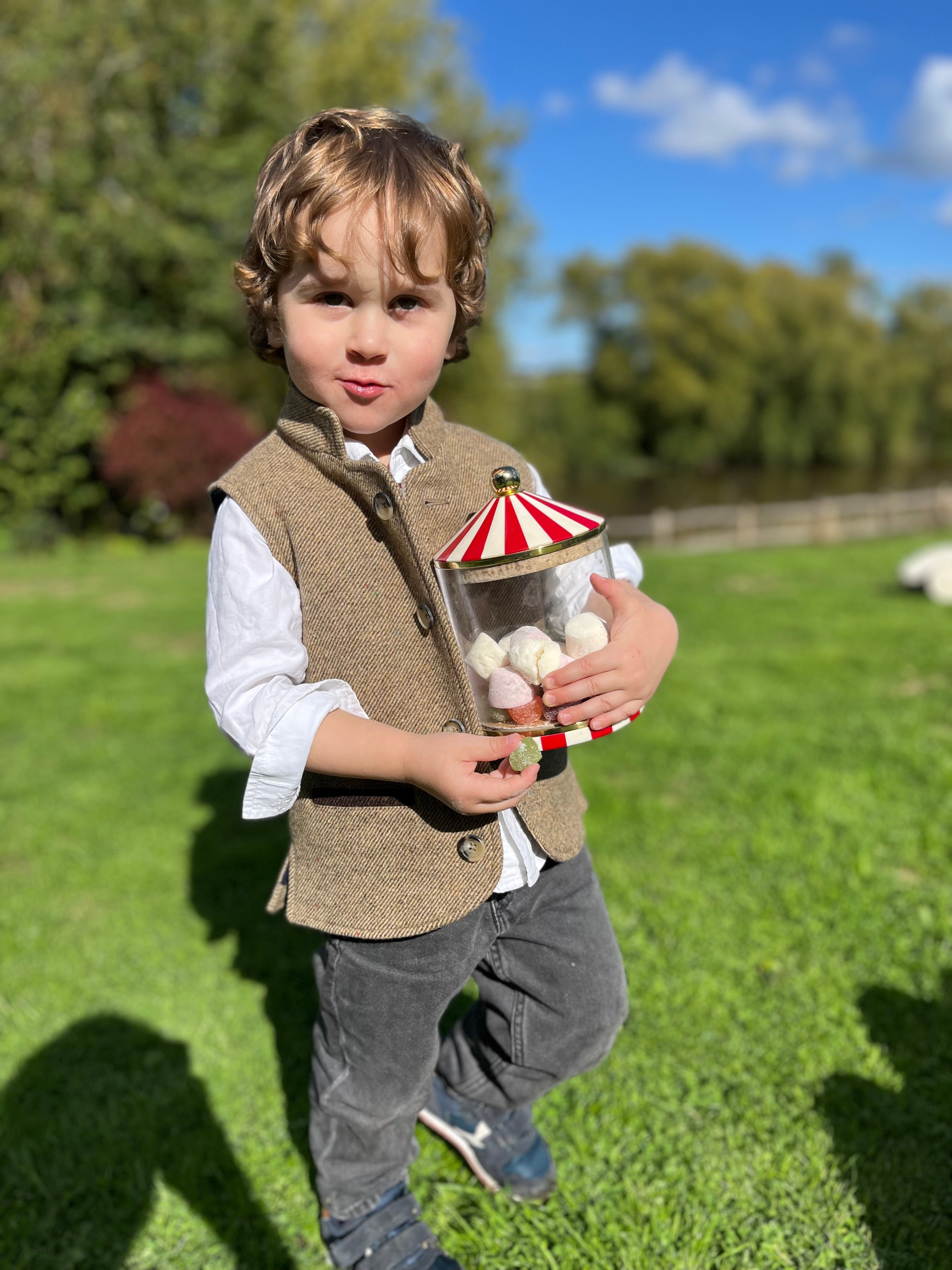 Boy wearing Little Darzi gilet in Camel Brown holding candy jar